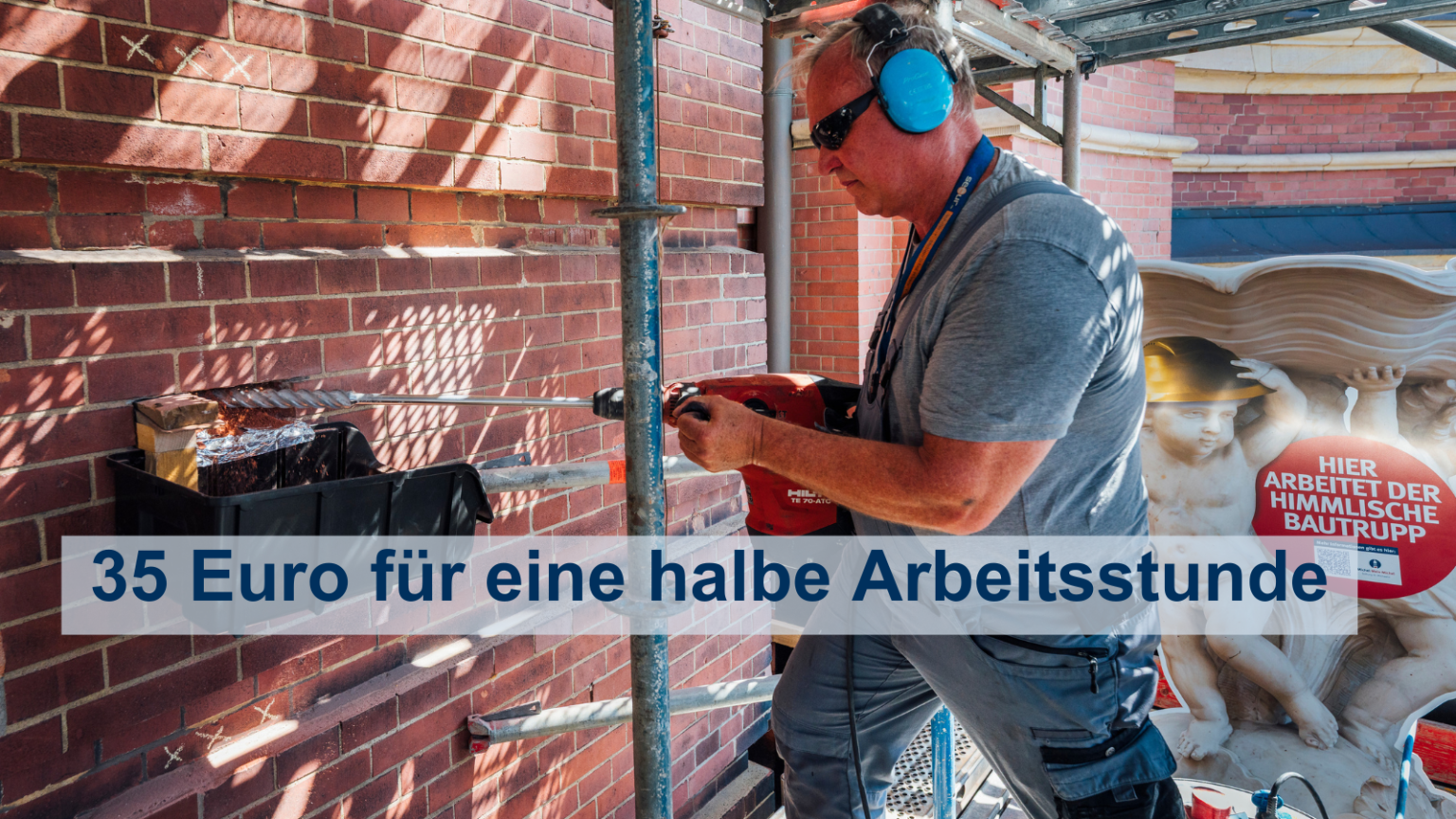 Auf einem Baugerüst steht ein Handwerker mit Gehörschutz und bohrt in dem Michel-Turm ein Loch.