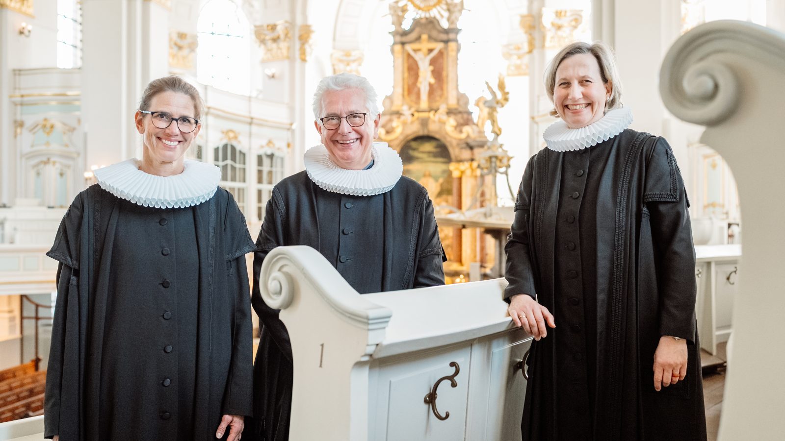Pastorin Julia Atze, Hauptpastor Alexander Röder und Pastorin Corinna Senf stehen im Talar auf der Empore des Michel, Im Hintergrund ist der Altarraum zu sehen