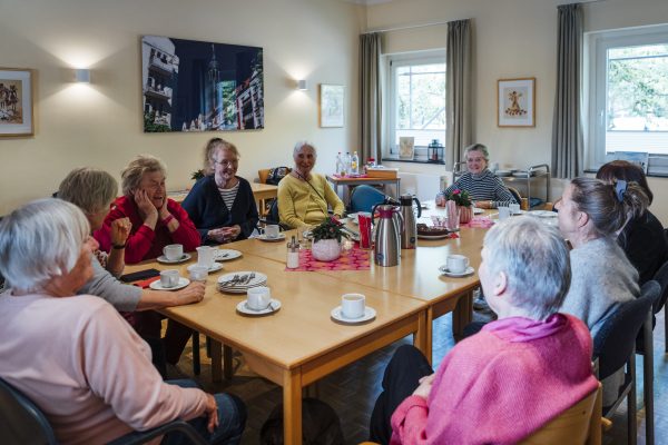 Frauen des Michel-Treffs sitzen am mit Kaffee und Kuchen gedeckten Tisch und unterhalten sich.