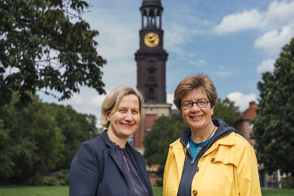 Pastorin Corinna Senf und Diakonin Anke Frickmann auf der Michel-Wiese. Im Hintergrund ist der Michel zu sehen.