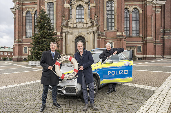 Polizeipräsident Ralf Martin Meyer und Ehrenkommissar Marek Erhardt vor einem Polizeiauto auf dem Kirchplatz des Michel.