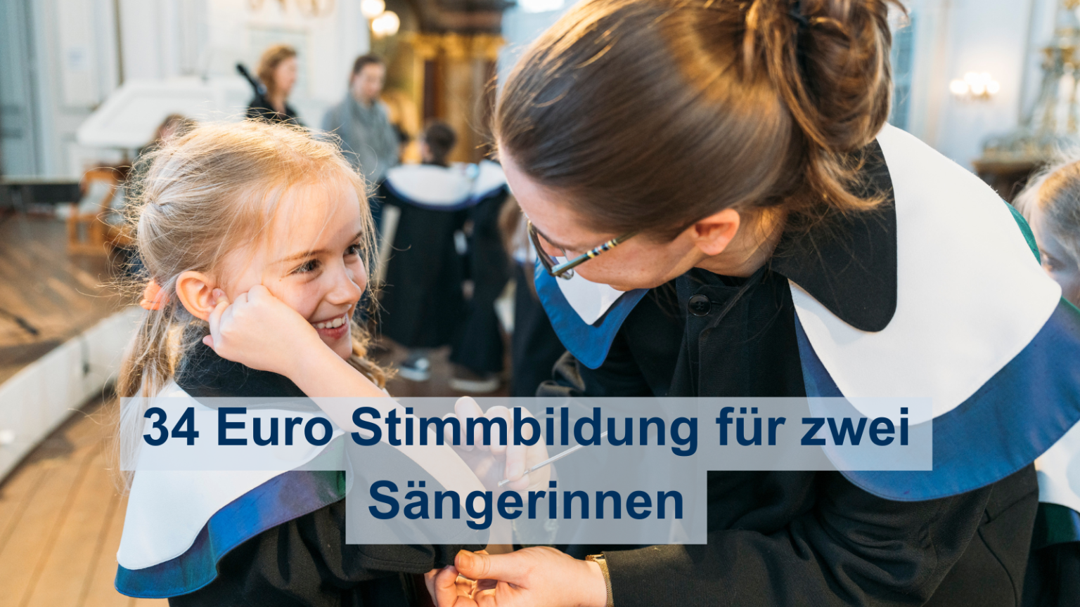 Eine Sängerin der Singschule bekommt von der Leiterin eine Stimmgabel an den Ellbogen getan.
