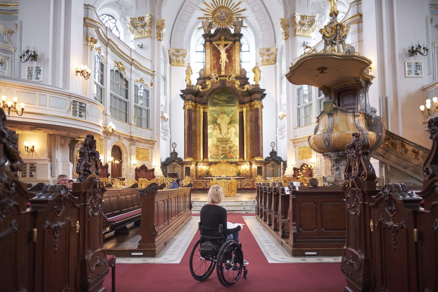Frau in Rollstuhl guckt auf den Hochaltar des Michel