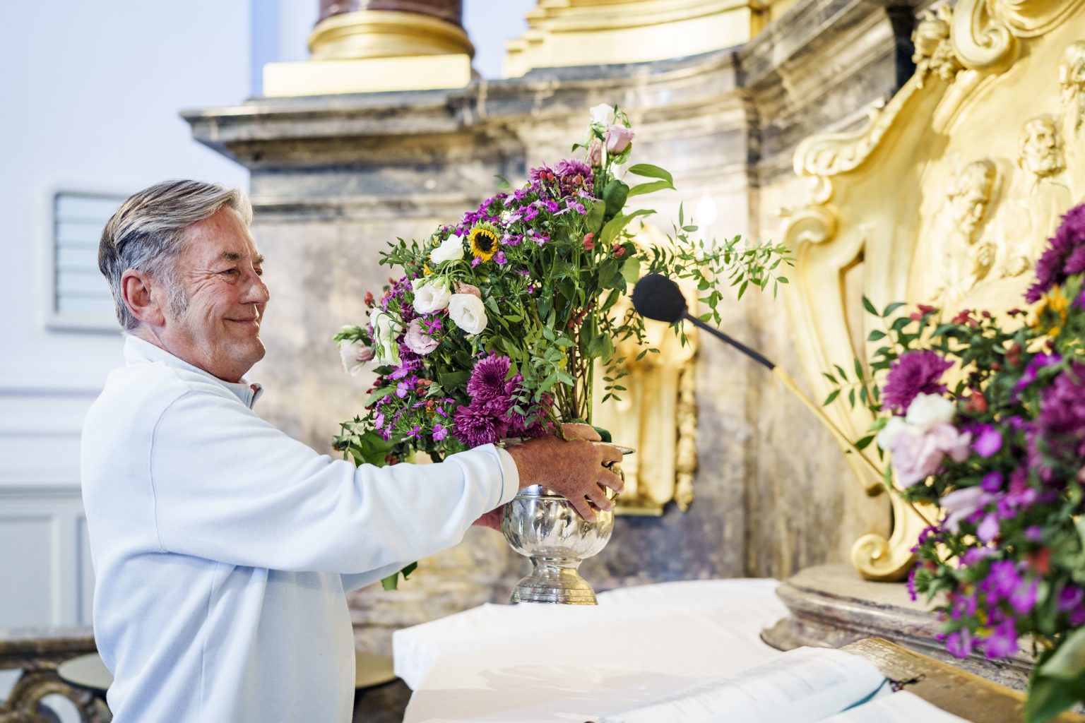 Ein Ehrenamtlicher des Michel stellt neue Blumen auf den Altar.