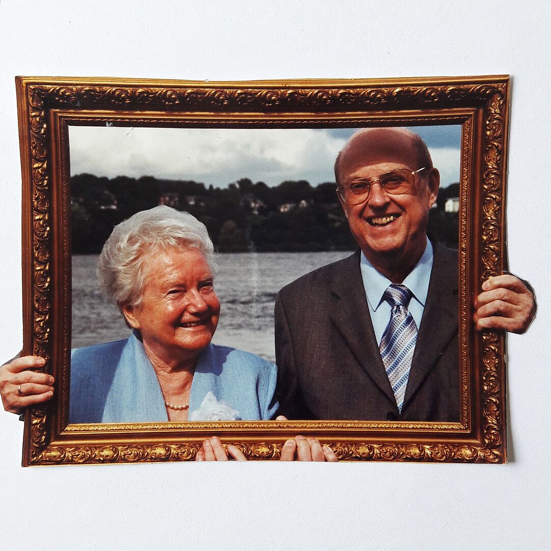 Das Ehepaar Hannelore und Georg Wiarda blicken lächelnd in die Kamera, vor sich einen goldenen Bilderrahmen haltend.