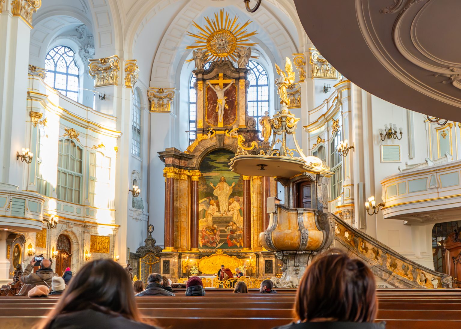 Besucher in den Kirchenbänken blicken auf den Hochaltar
